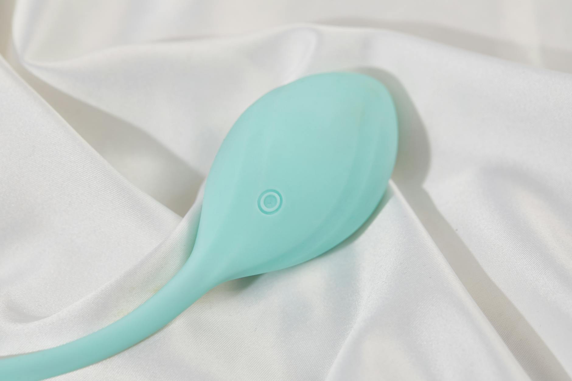 Ein stilvoller türkiser Vibrator auf glattem weißem Seidenstoff