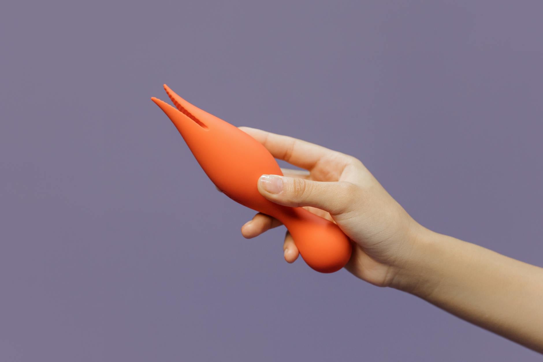 Eine Hand hält einen modernen Lemon-Vibrator mit Saugtechnik vor einem minimalistischen purpurnen Hintergrund