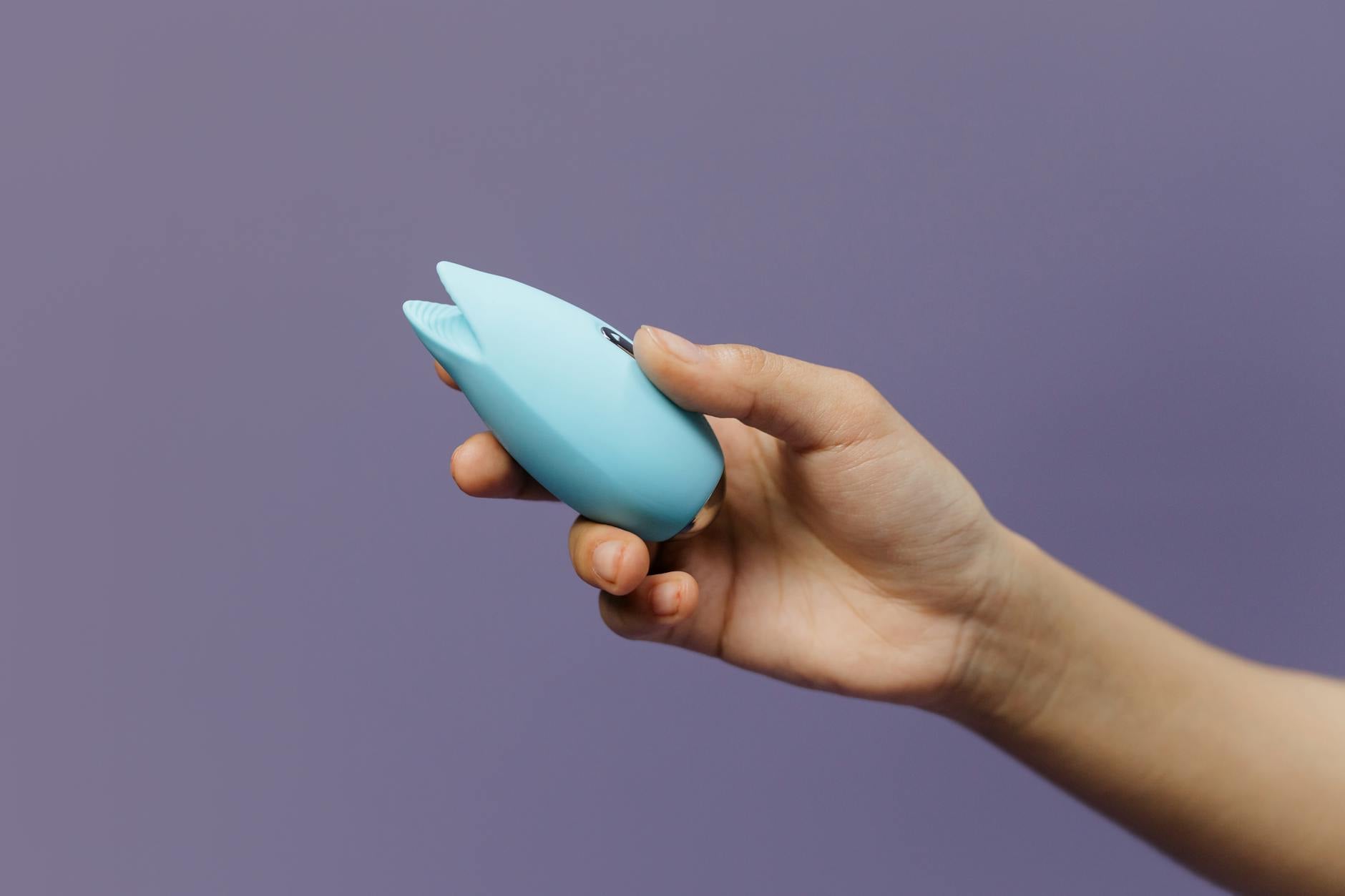 Eine Hand hält einen blauen Silikonvibrator vor einem festen violetten Hintergrund, Selbstliebe und Sexualität fördernd