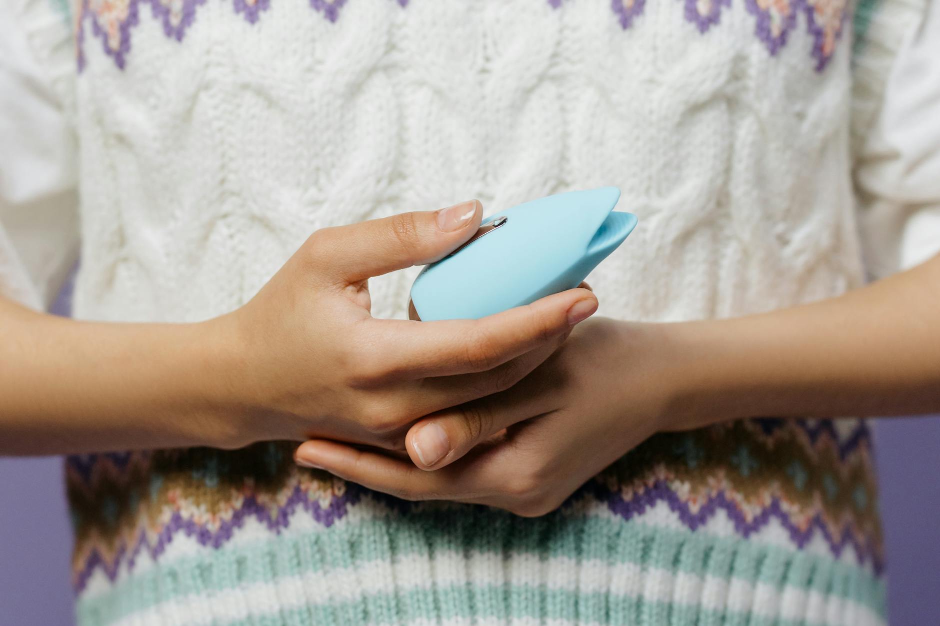 Nahaufnahme von Händen, die einen blauen Massagevibrator gegen einen gestrickten Pullover halten